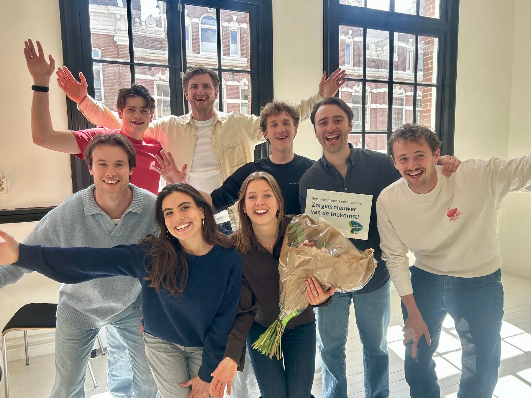 Het PAVA-team viert de nominatie op kantoor, met een bloemboeket en de kaart van VGZ: 'Gefeliciteerd met je nominatie als Zorgvernieuwer van de toekomst!'